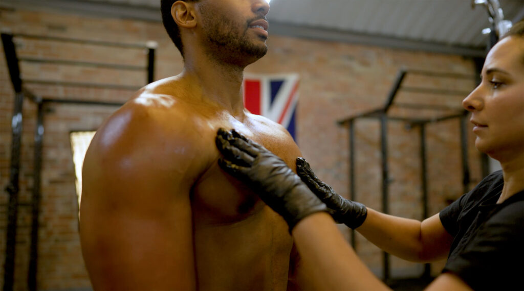 A model preparing for a photoshoot with a flawless spray tan, highlighting muscle definition and skin tone.